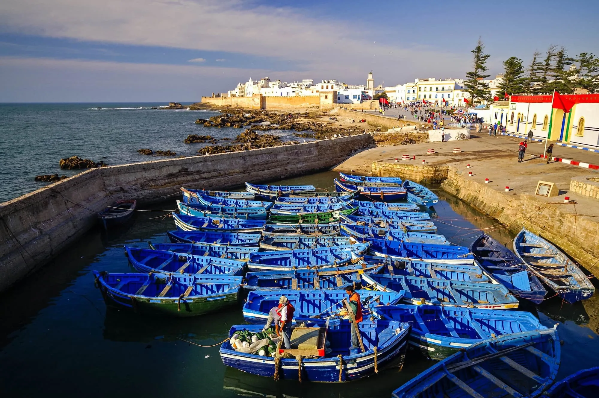 Traditional blue fishing boats in Essaouira harbor with white medina buildings in background