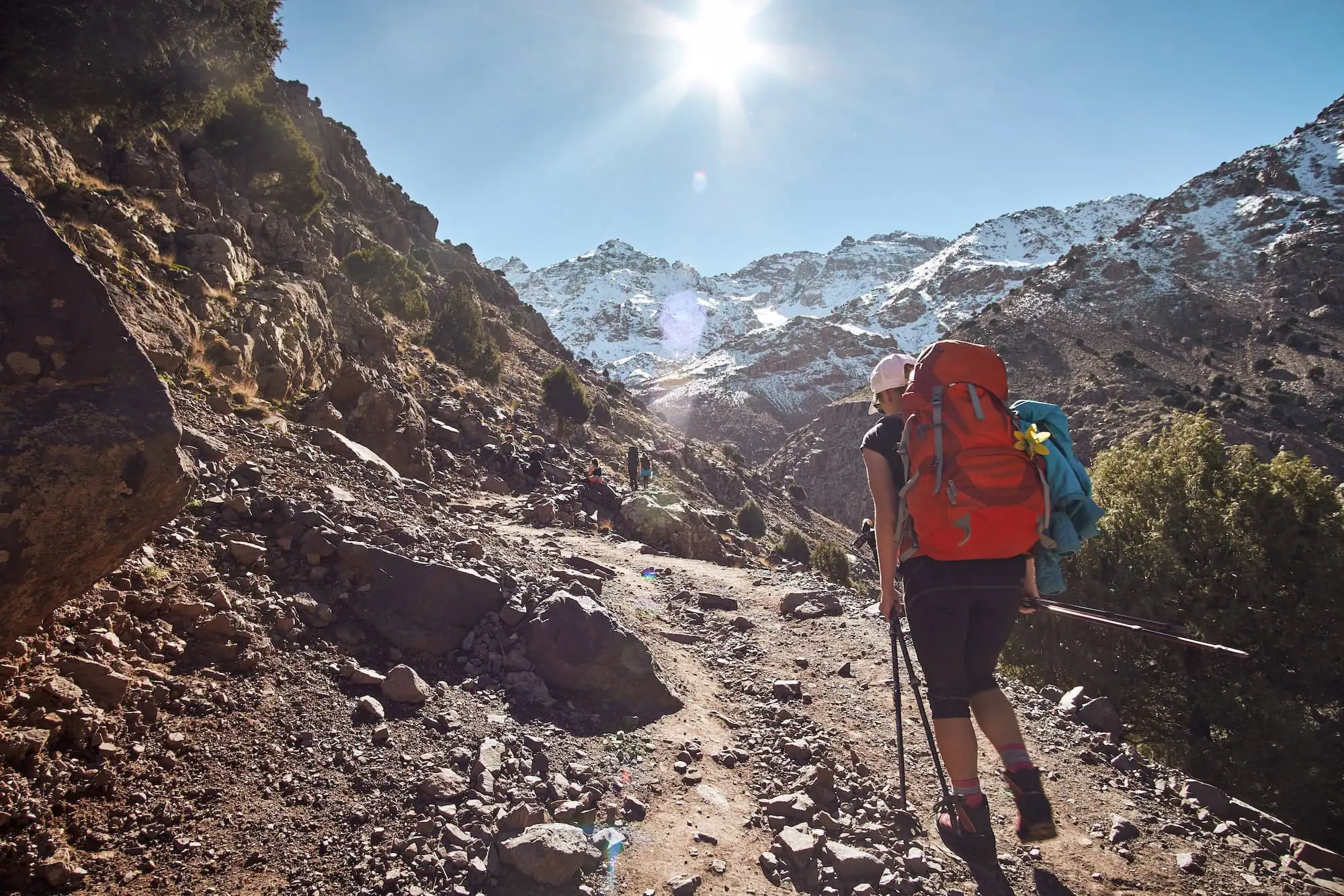 Female backpacker hiking on mountain trail in Morocco's Atlas mountains with snow-capped peaks