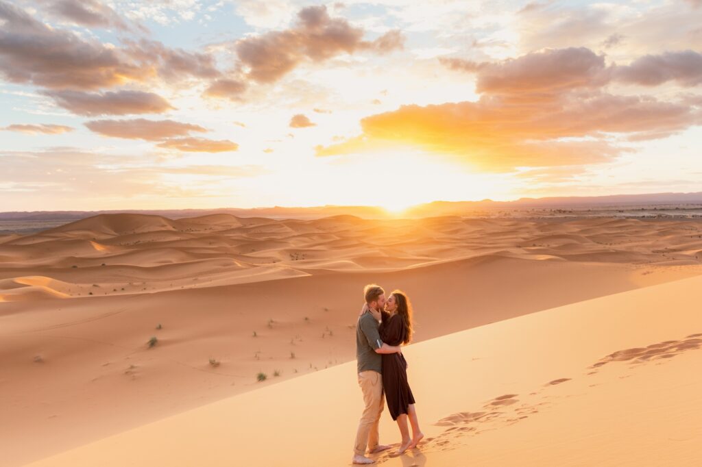 Young couple walking together across Sahara dunes at sunset