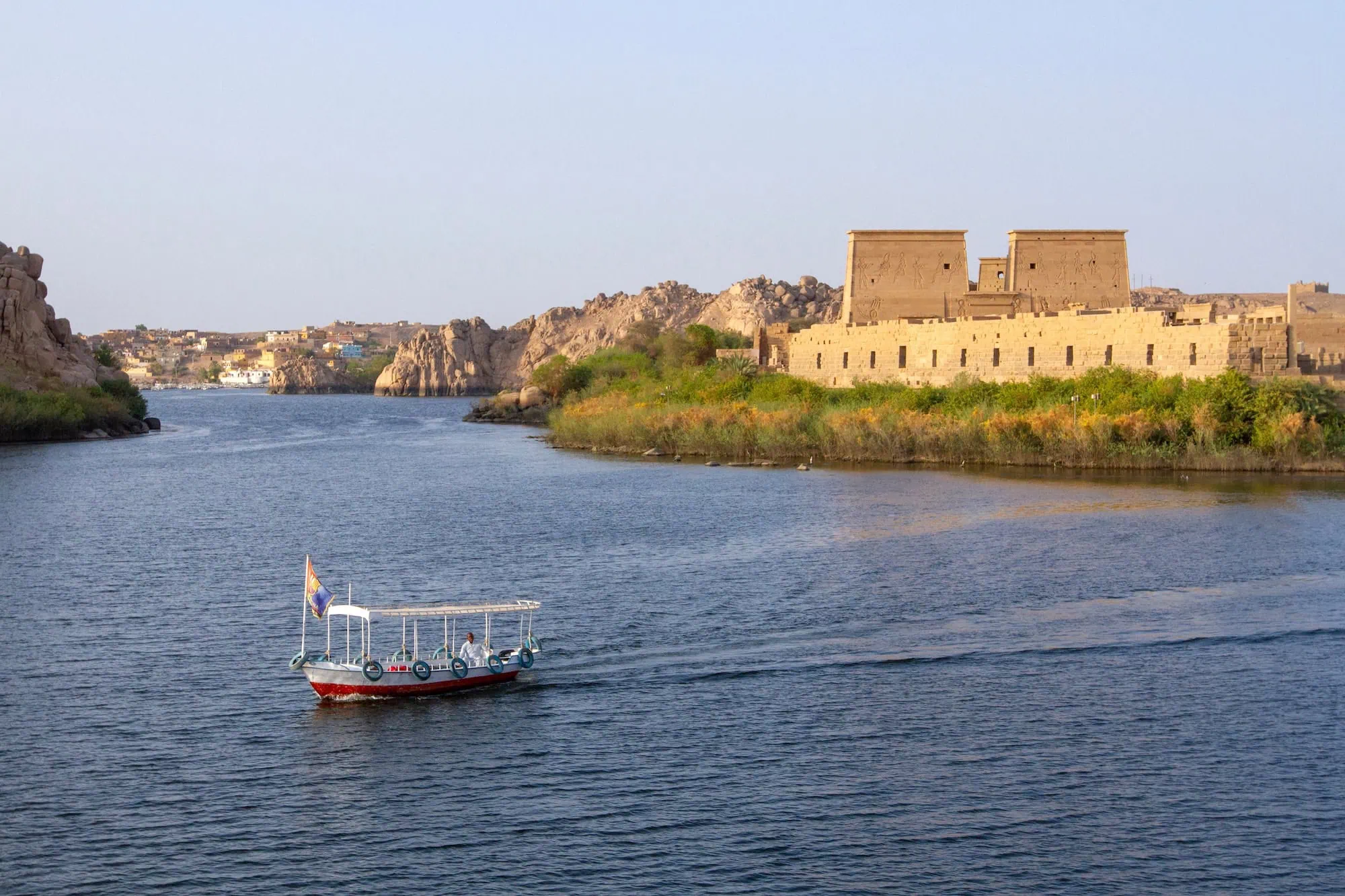 Tourist boat approaching the ancient Philae Temple complex on the Nile River in Aswan, Egypt