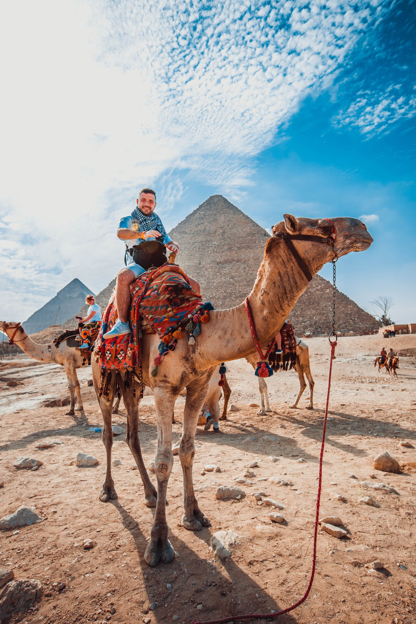 Tourist riding camel with decorative saddle blanket at Pyramids of Giza