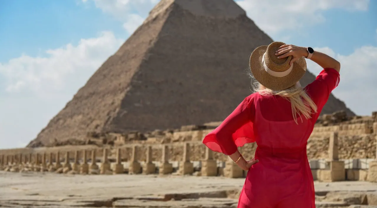 A girl in a red dress looks at an Egyptian pyramid.
