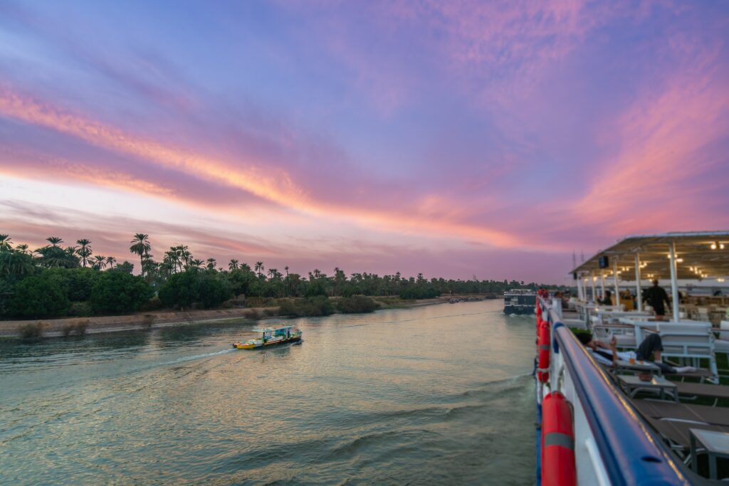 A cruise boat deck overlooking the calm river as warm sunset colors reflect on the water, Nile River, Esna