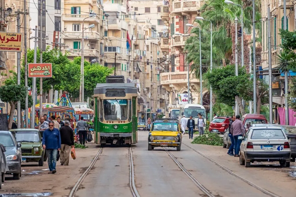 Busy street with pedestrians, trams, and older model cars in the city center, Alexandria