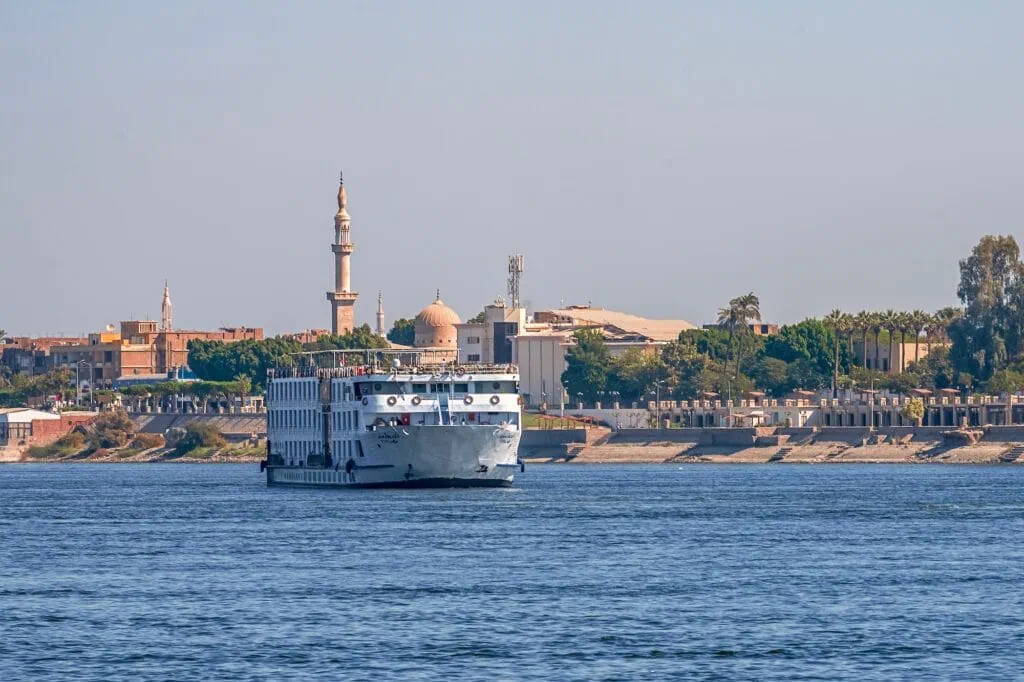 Large cruise ferry sailing on the Nile River with Aswan cityscape in the background, Aswan
