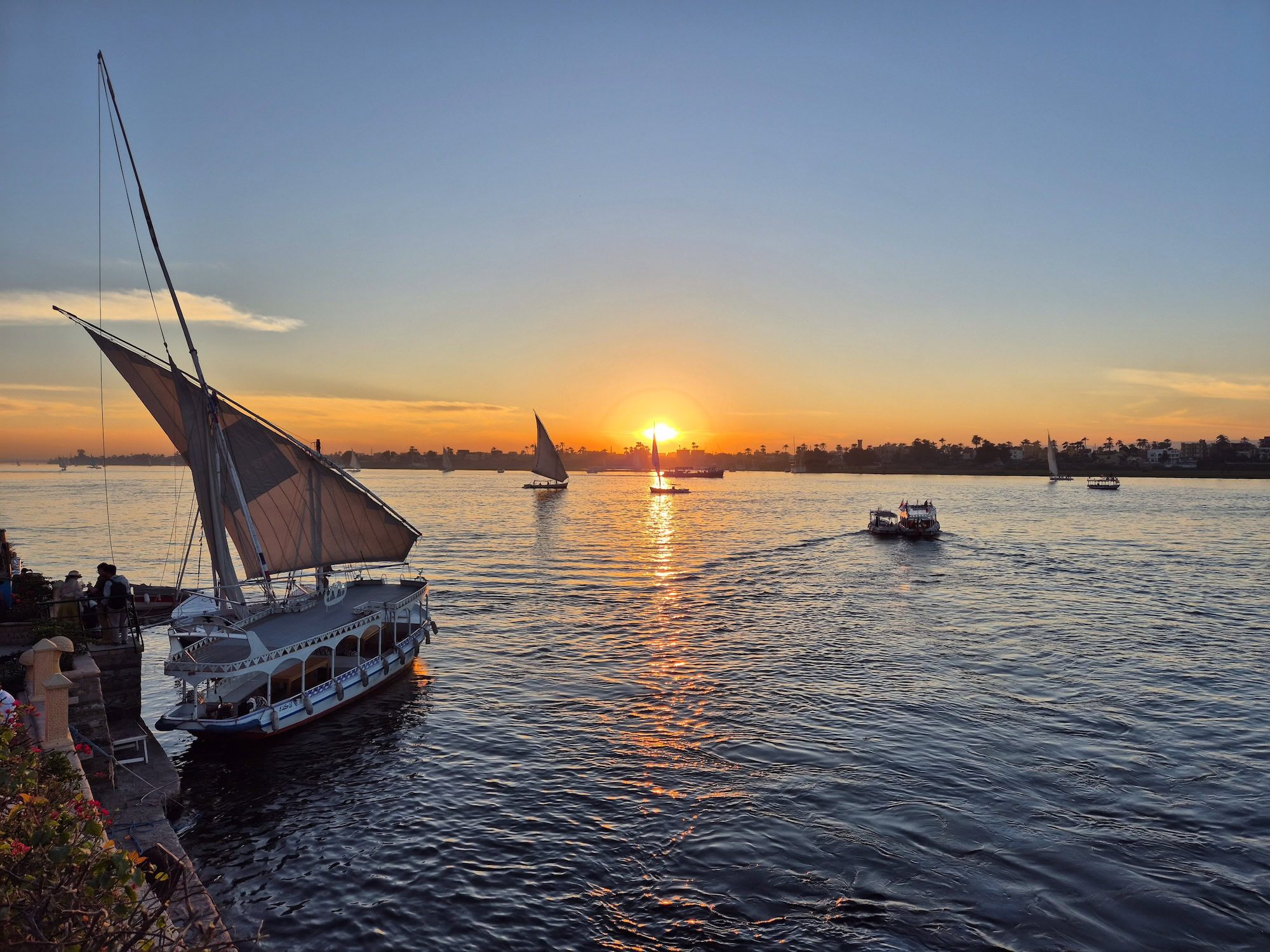 Traditional felucca sailboat on the Nile River at sunset with panoramic river views
