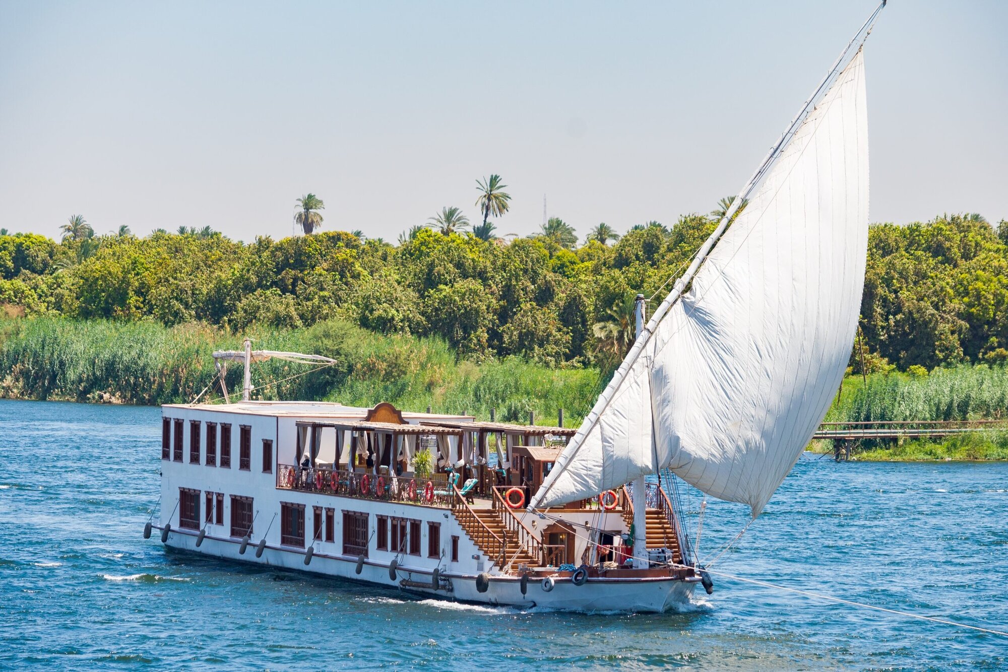 Traditional white-sailed dahabiya cruise boat on the Nile River with tourists on deck