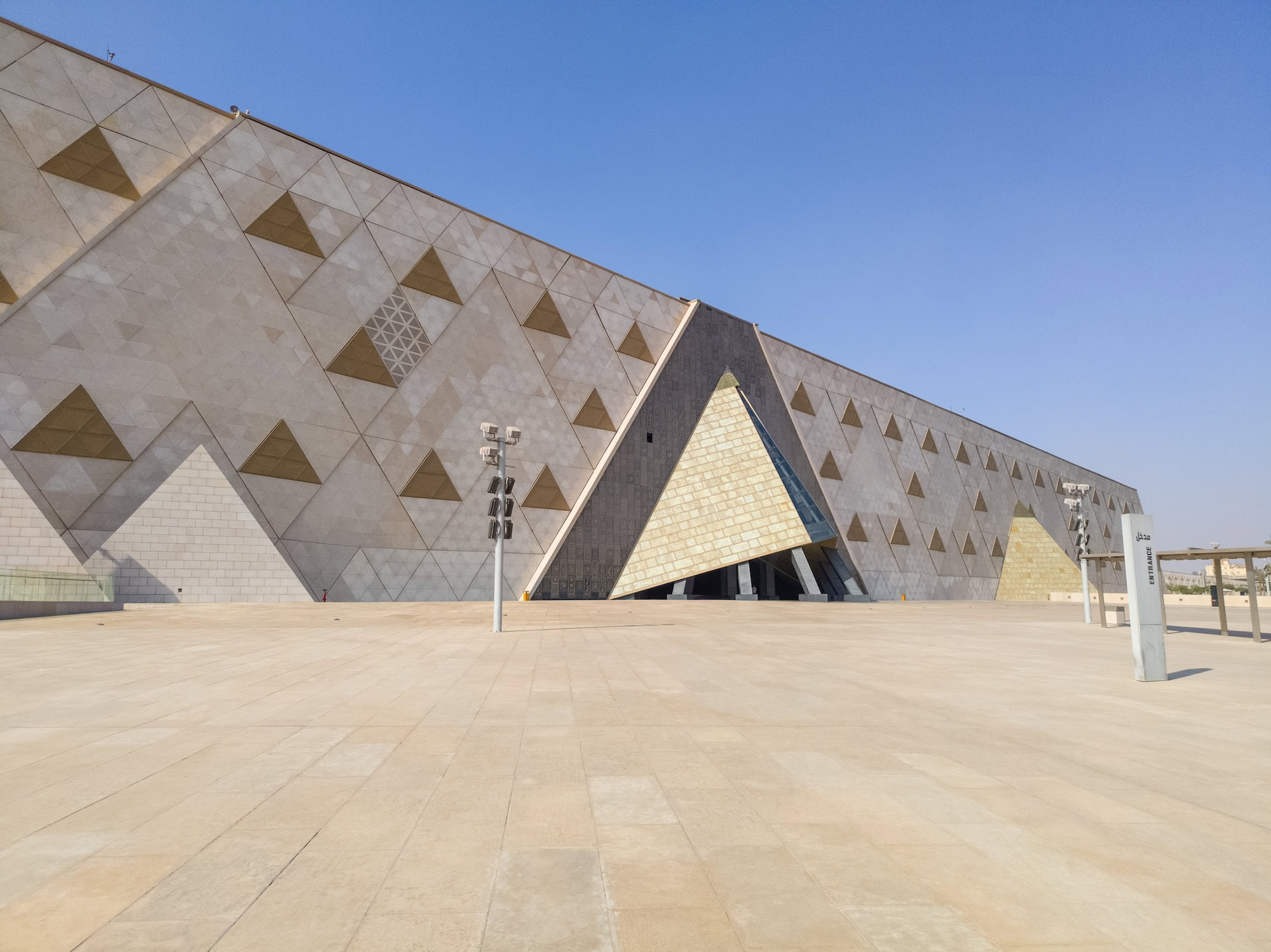 Grand Egyptian Museum exterior with triangular facade and stone plaza in Giza
