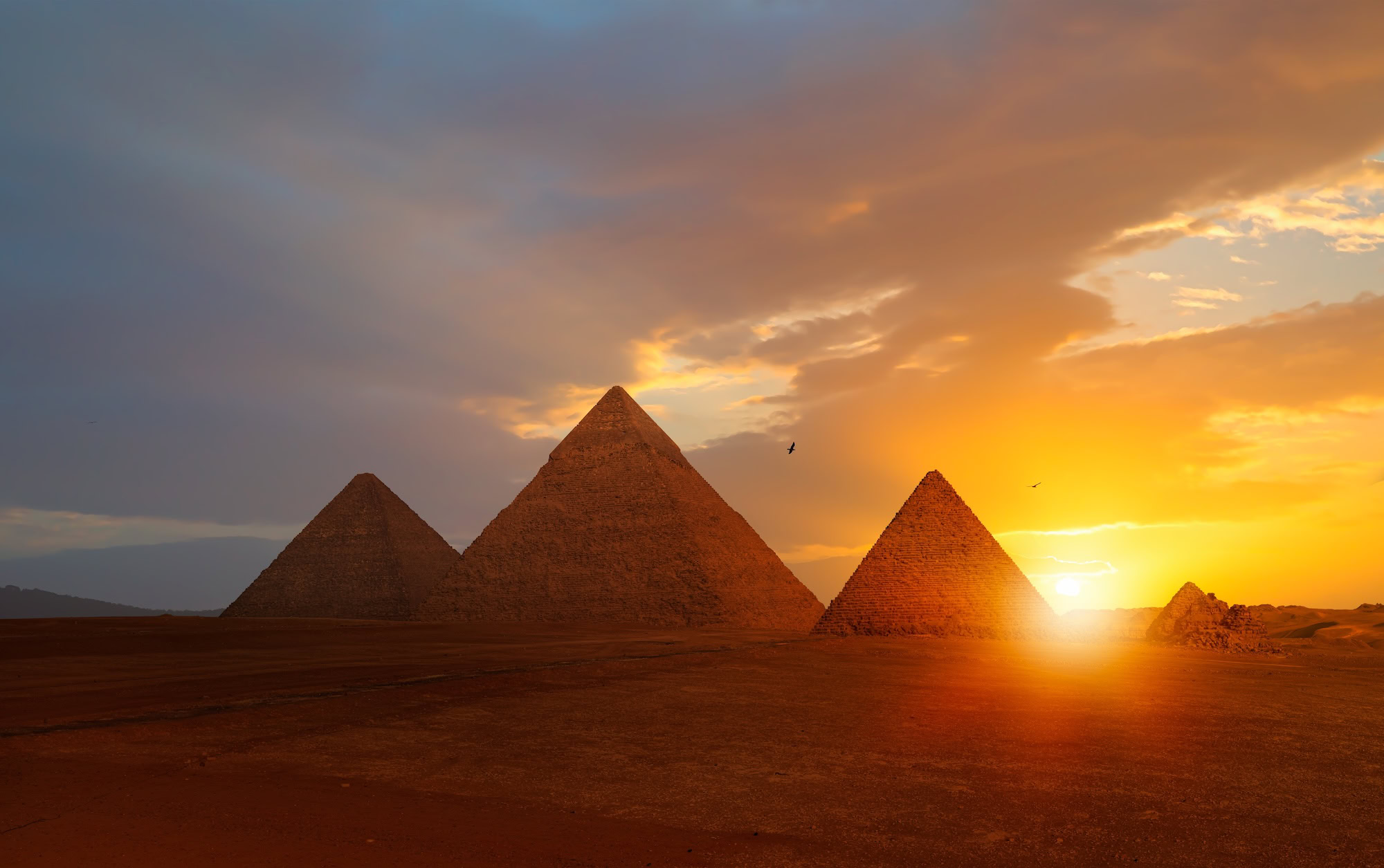 Great Pyramids of Giza at sunrise with desert landscape and cloudy sky