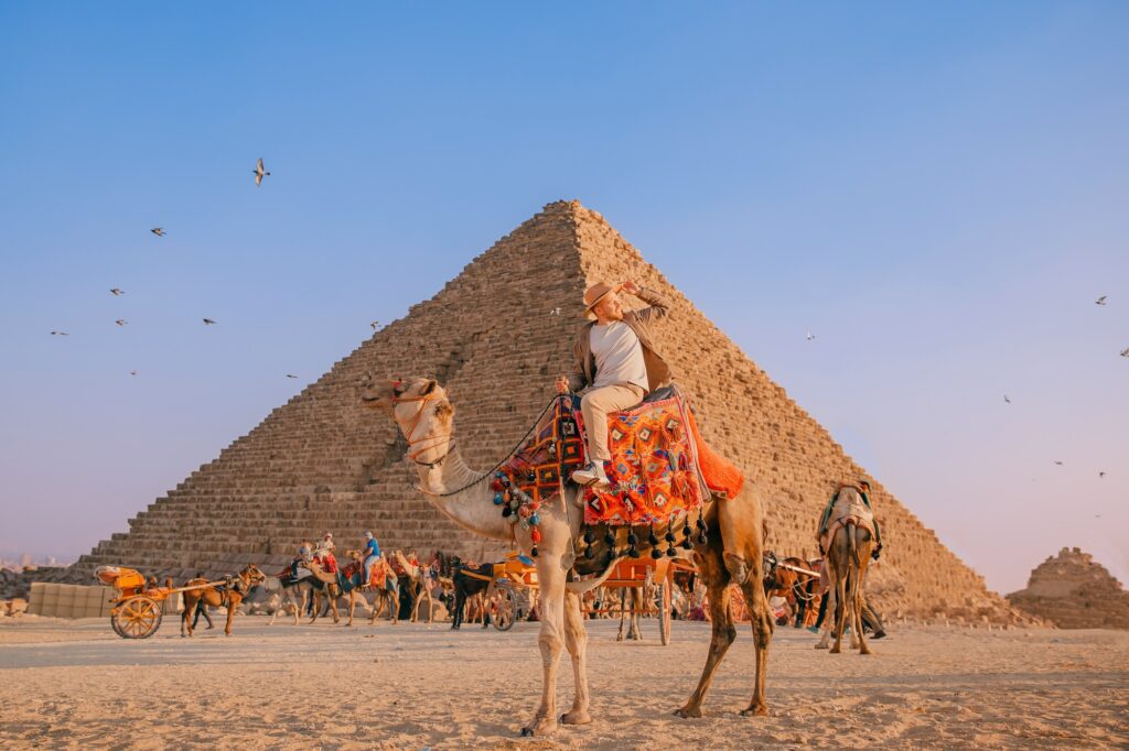 Happy tourist riding a camel with Giza pyramids in the background