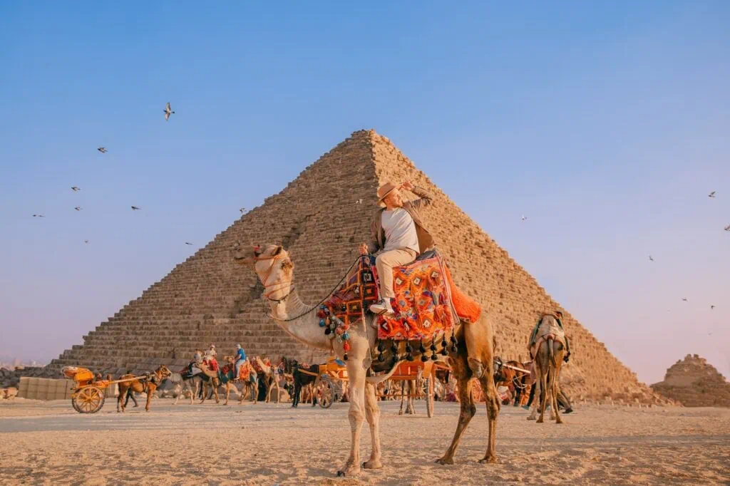 Happy tourist riding a camel with Giza pyramids in the background