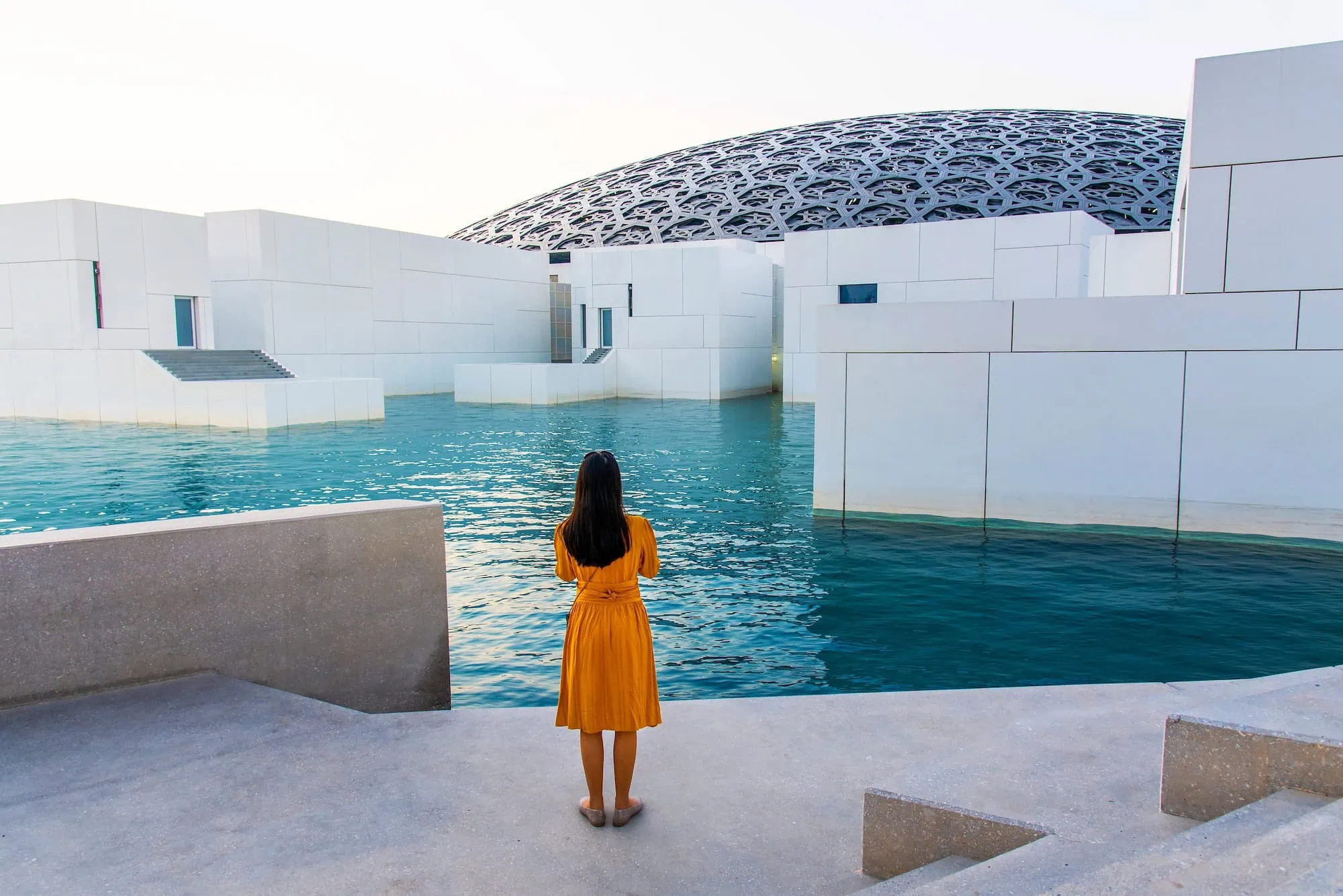 Louvre Abu Dhabi's geometric dome with woman walking beneath intricate light patterns