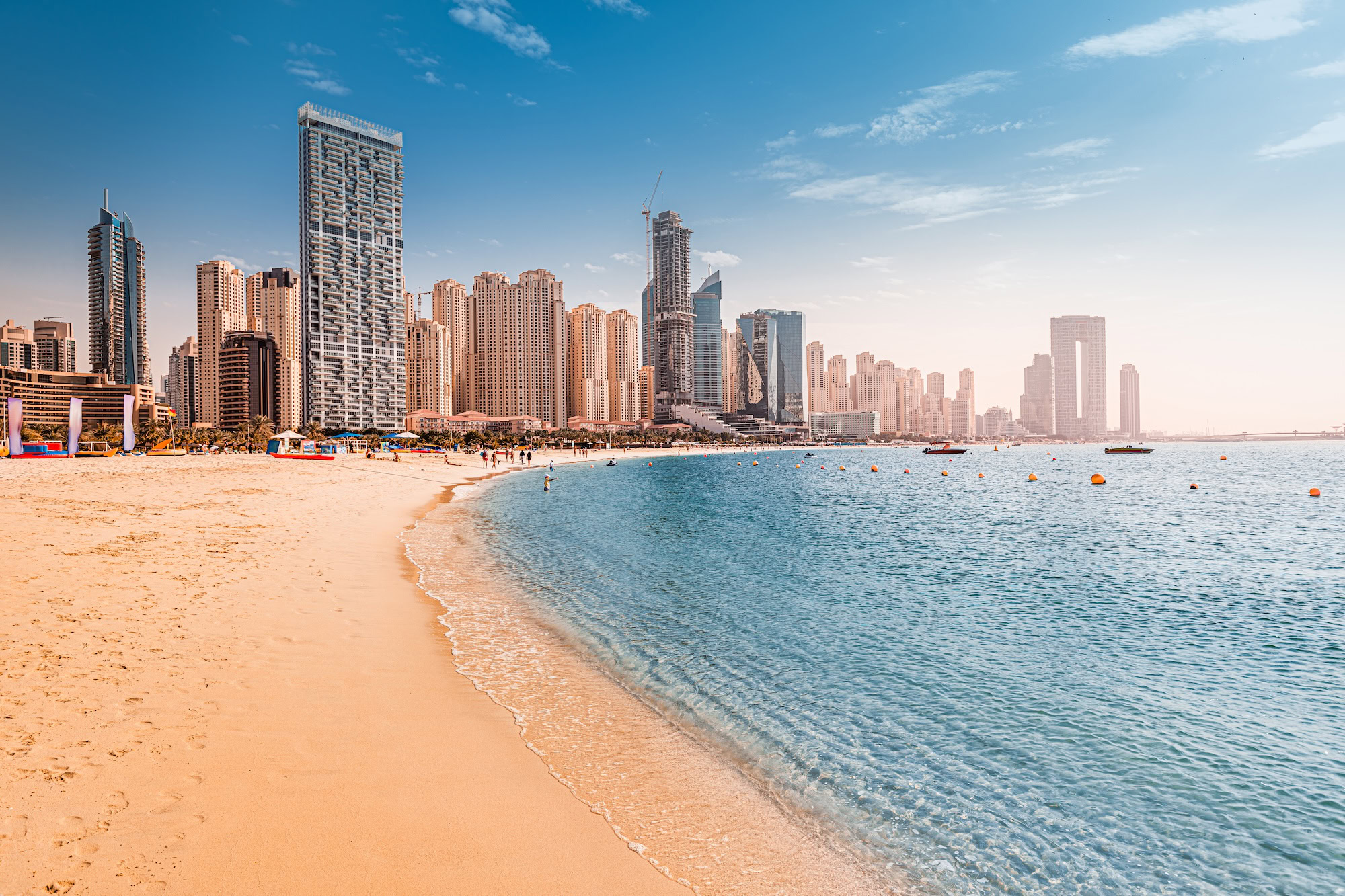 Praia de Dubai com arranha-céus ao fundo, água cristalina e atividades aquáticas