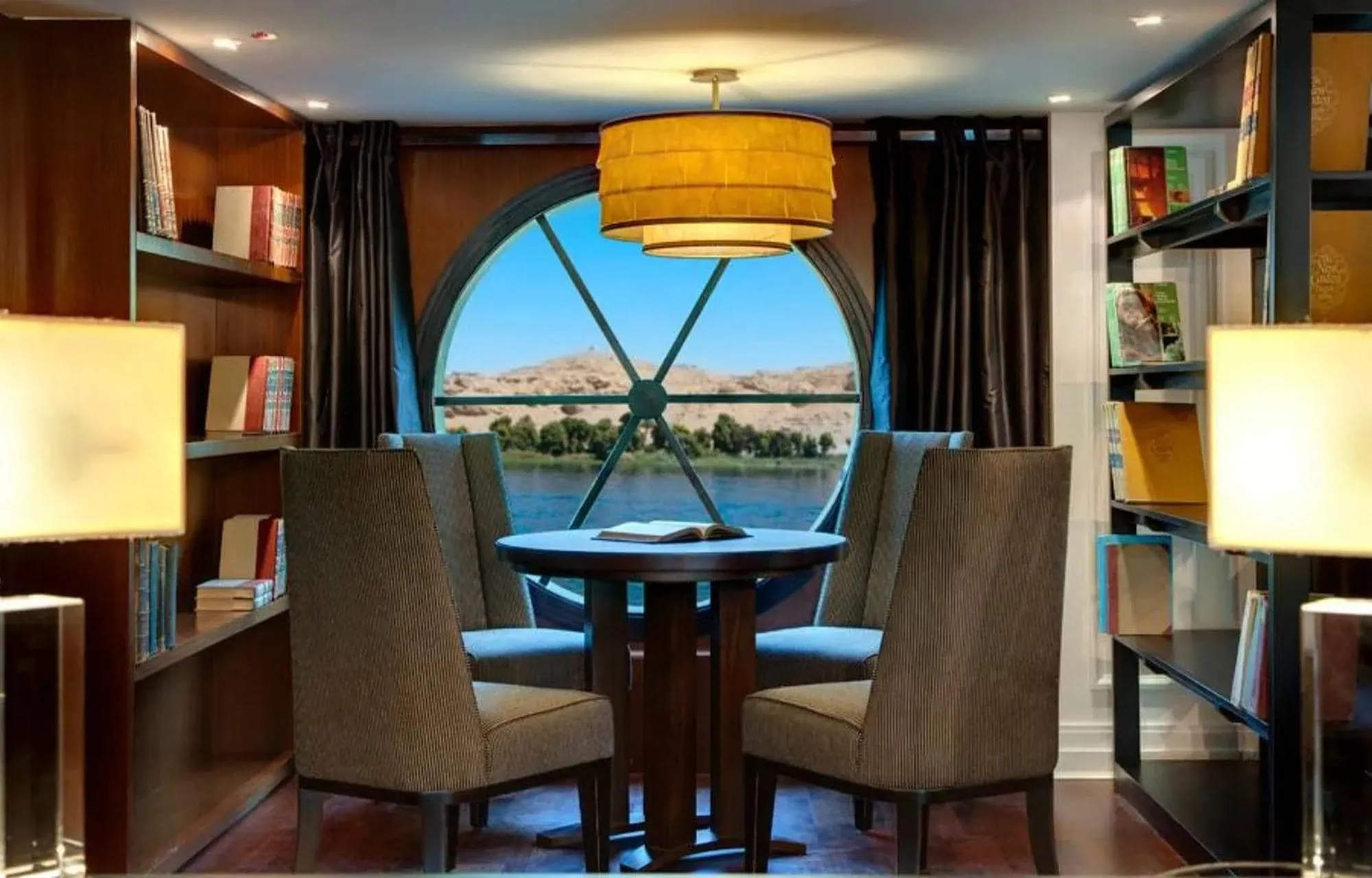 Luxurious cruise ship cabin with elegant furniture and round window overlooking Nile River desert landscape
