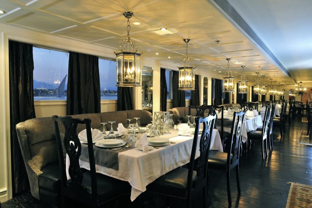 Elegant onboard restaurant with dining tables, large windows, and river views on the Mayfair Nile Cruise, Luxor