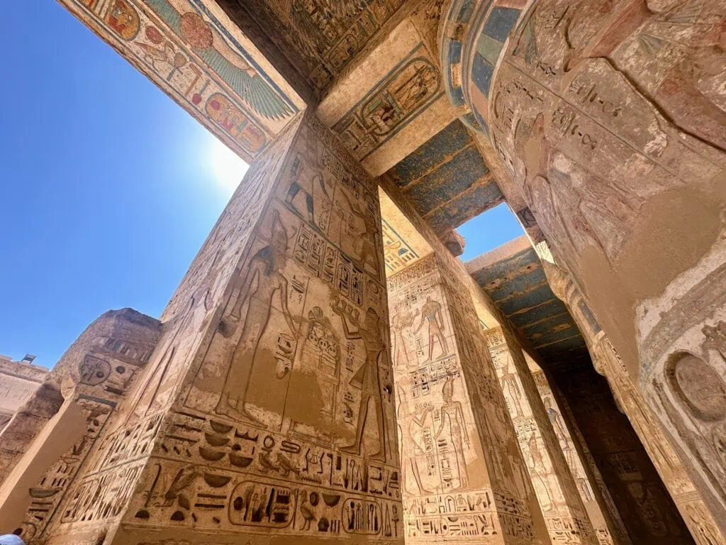 Upward view of blue-painted ceiling and decorated stone columns inside the Temple of Medinet Habu, Luxor