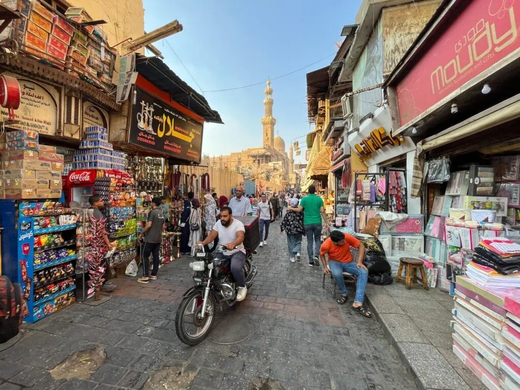 Street view of Khan el-Khalili market with local shops, pedestrians, and a mosque minaret in the background, Khan el-Khalili, Cairo