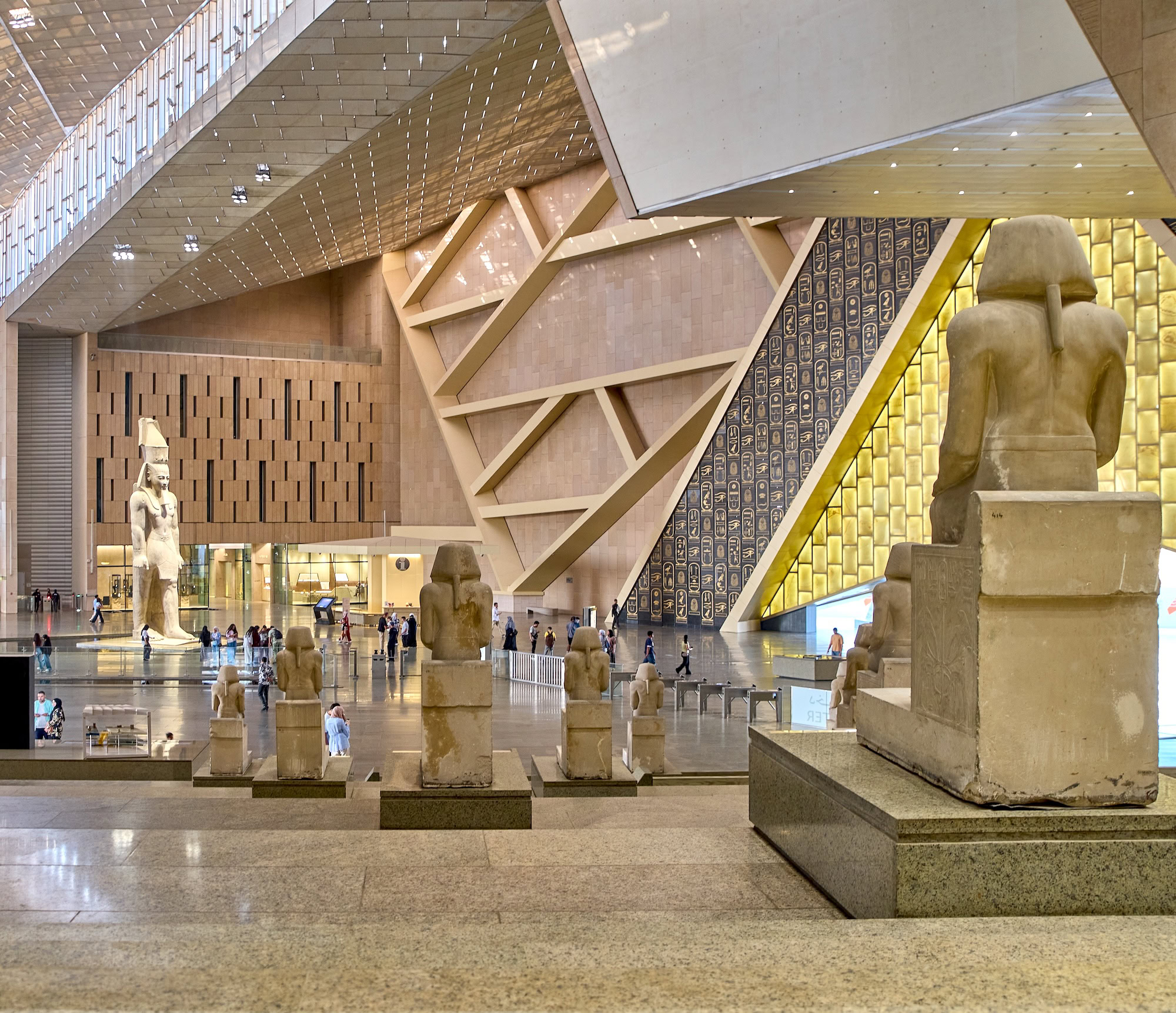 Visitors exploring ancient Egyptian artifacts and statues in the Grand Egyptian Museum interior