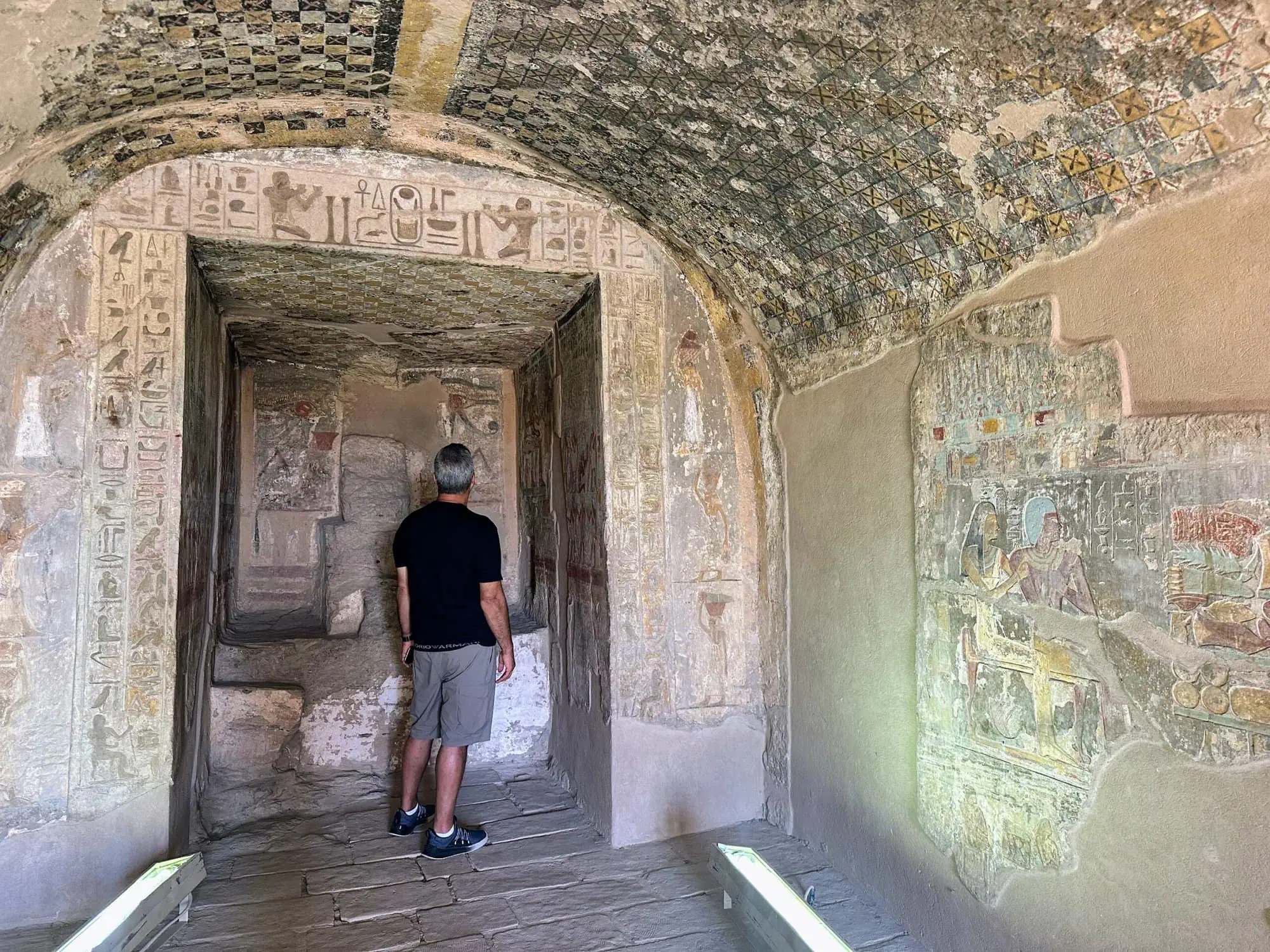 Interior of Egyptian tomb showing hieroglyphs and painted ceiling with visitor inside