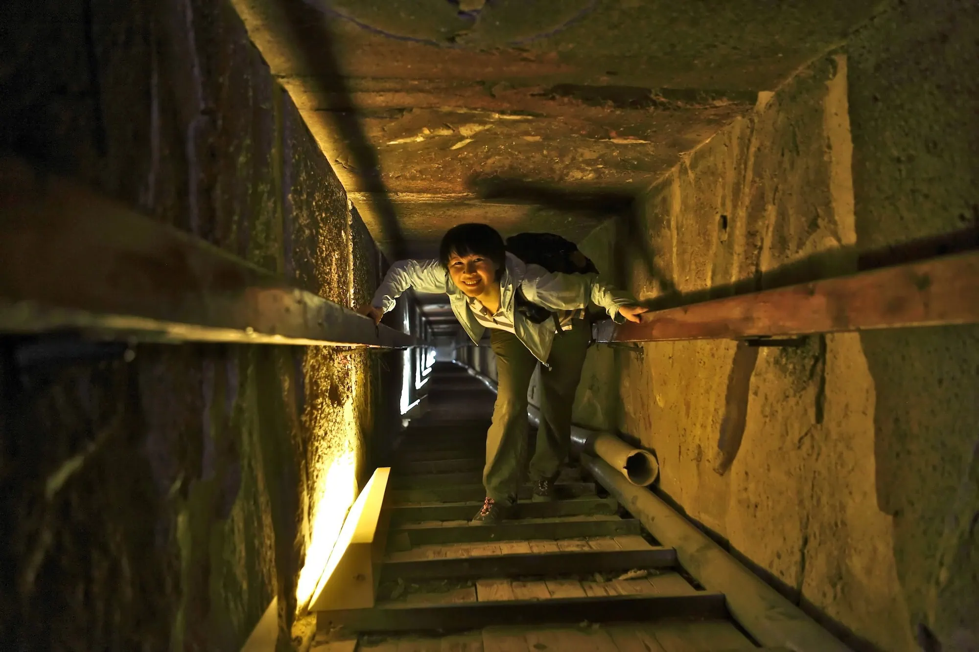 Tourist exploring narrow stone passage inside Great Pyramid with ancient limestone walls