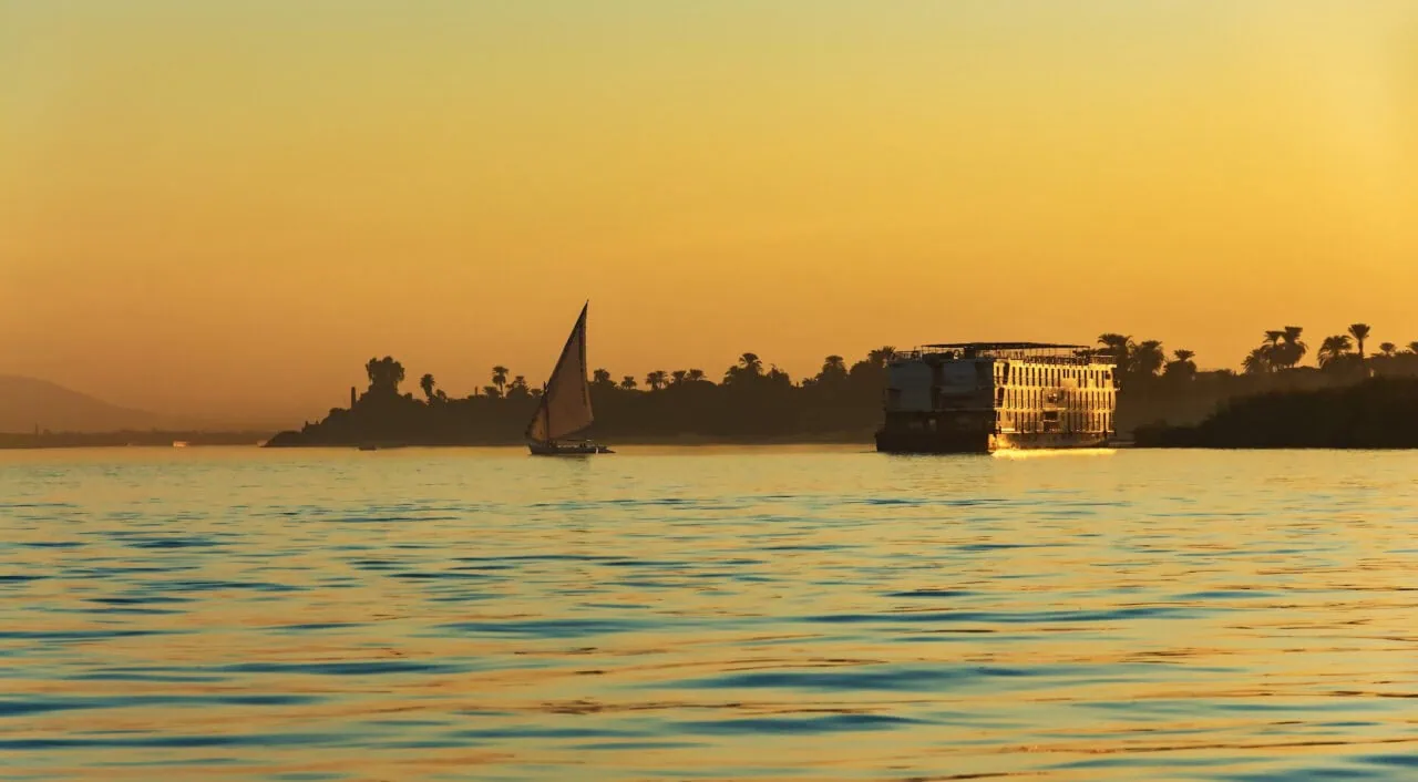 Traditional sailboat and cruise ship on the Nile River at sunset in Luxor, Egypt with golden sky reflection