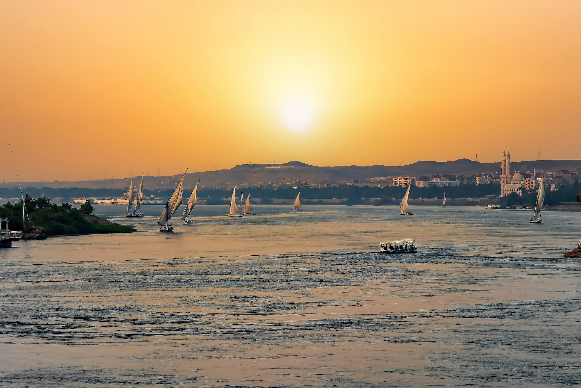 View of a beautiful orange sunset in Aswan Egypt with a lot of felucca sailing in the Nile river