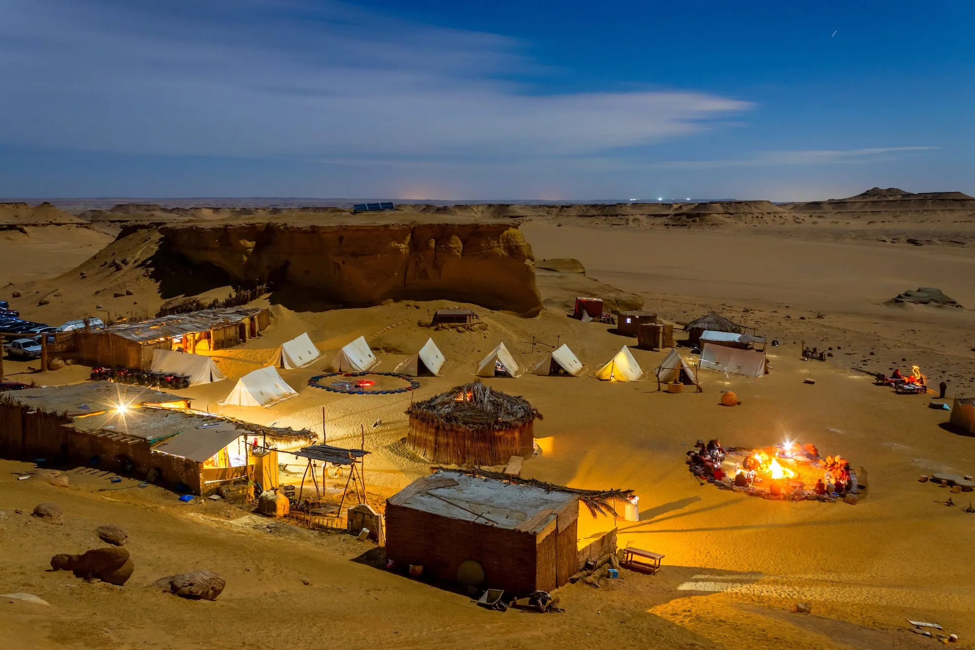 Campamento en el desierto del Sahara con tiendas iluminadas y fogata bajo el cielo nocturno
