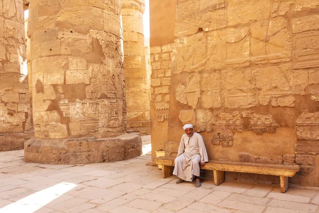 Egyptian man in traditional dress sitting near the stone columns of Luxor Temple, Luxor