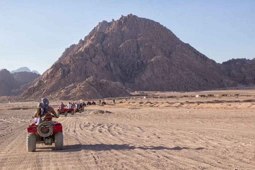Off-road quad bikes crossing a sandy desert plain with rocky mountains in the background at South Sinai Desert, Sharm El Sheikh