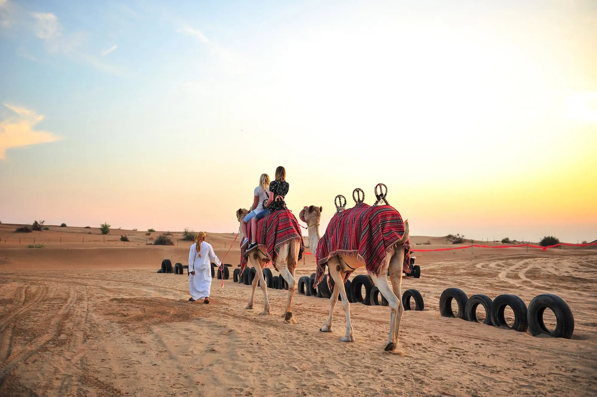 Camels and people in Dubai desert with traditional blankets during safari experience