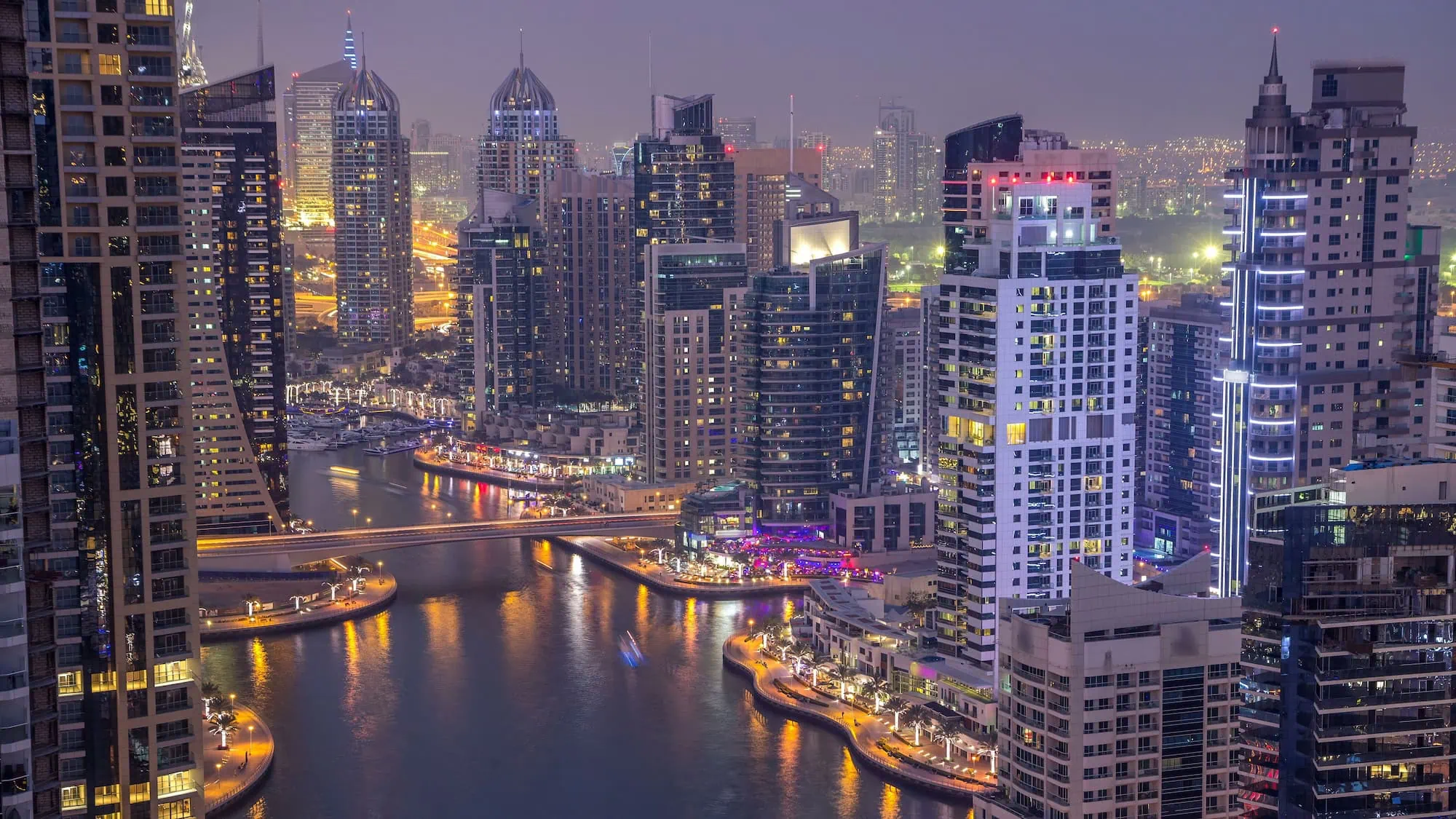 Illuminated Dubai Marina skyline at night with boats in the waterway