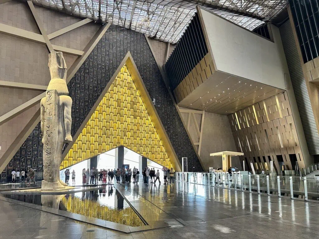 Interior view of the main hall with towering atrium, stone surfaces, and large statues at the Grand Egyptian Museum, Giza