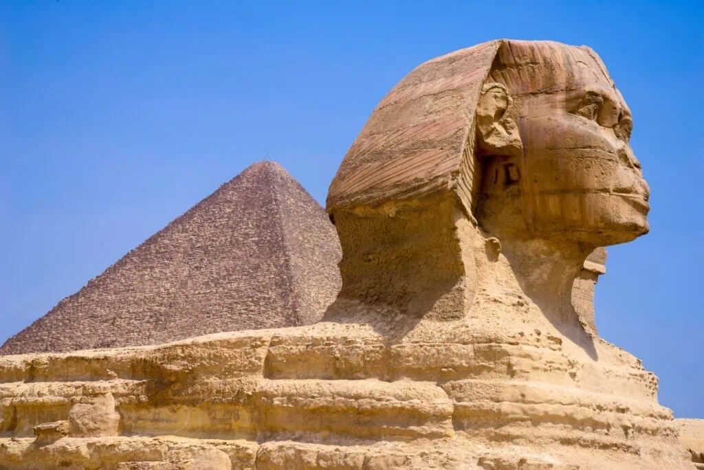 The Great Sphinx carved from limestone with the Giza pyramids plateau in the background, Giza