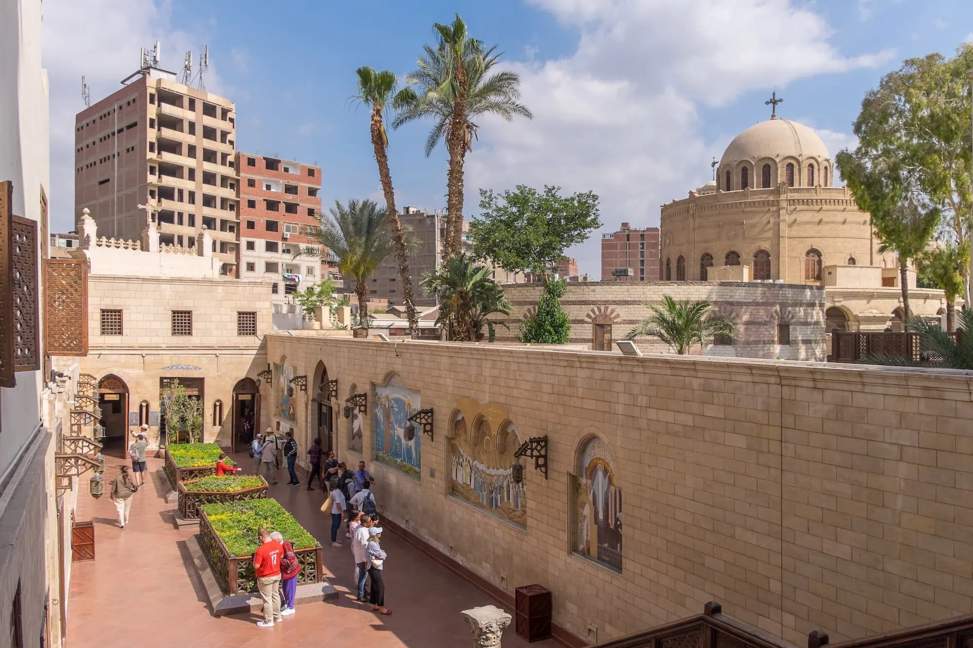 Historic Coptic Cairo courtyard with stone buildings, palm trees, and Christian cross