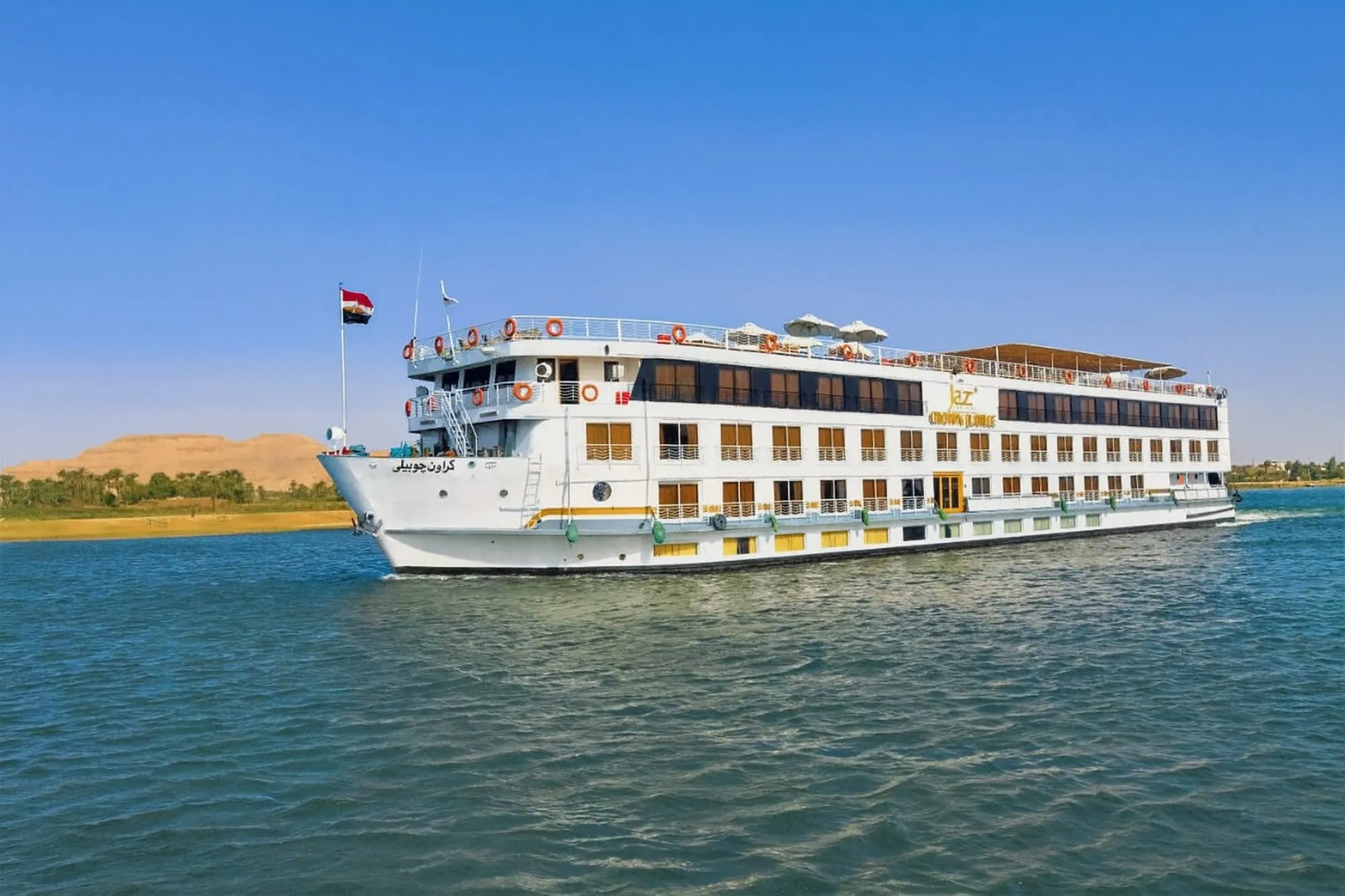 Crucero por el río Nilo navegando junto a dunas del desierto con bandera egipcia