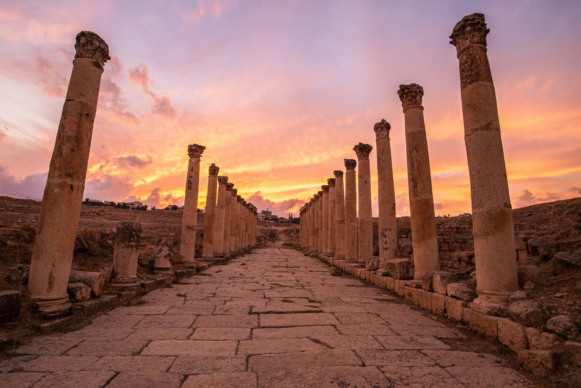 Ancient Roman columns with Corinthian capitals at Jerash archaeological site under dramatic sunset sky