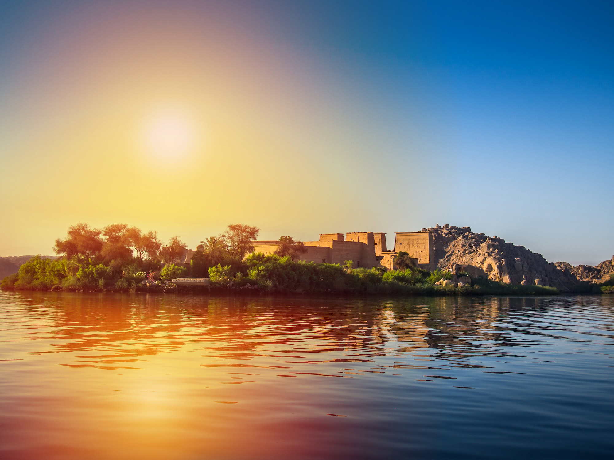 Philae Temple on small island surrounded by Nile waters with palm trees and ancient ruins