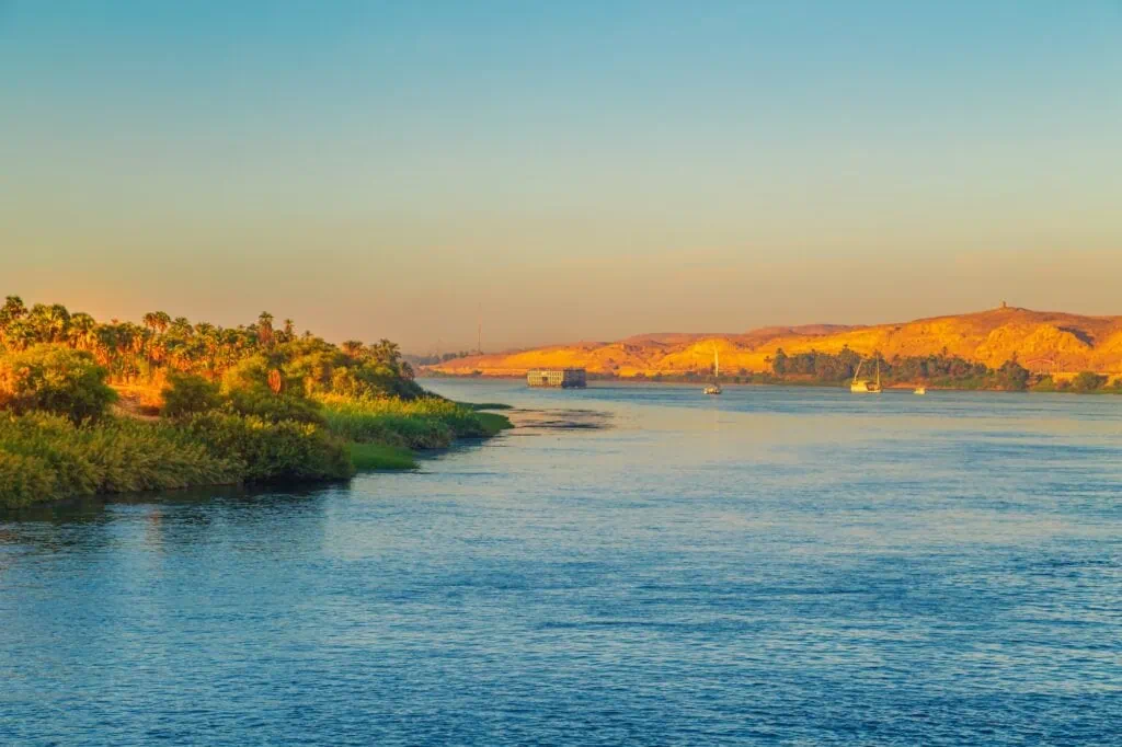 Sunlit Nile waters with lush riverbank palms and distant sandy hills