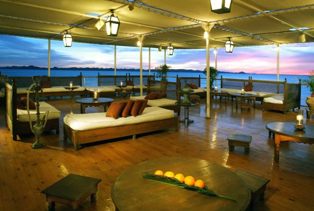 The spacious upper sun deck of the Movenpick Prince Abbas cruise ship with rows of loungers and shade umbrellas, sailing on Lake Nasser.