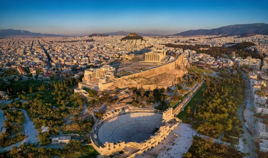 Aerial view of the Parthenon and the Odeon of Herodes Atticus on the Acropolis of Athens, Greece, in golden sunset light.
