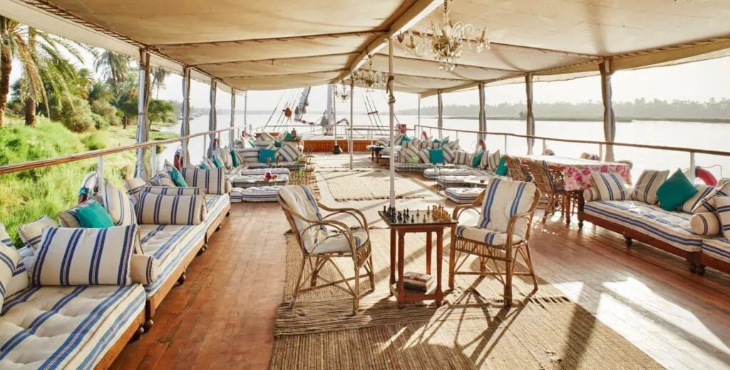 Sun deck of Nour El Nil Dahabiya with lounge seating, shaded canopy, and views of the Nile River, Aswan