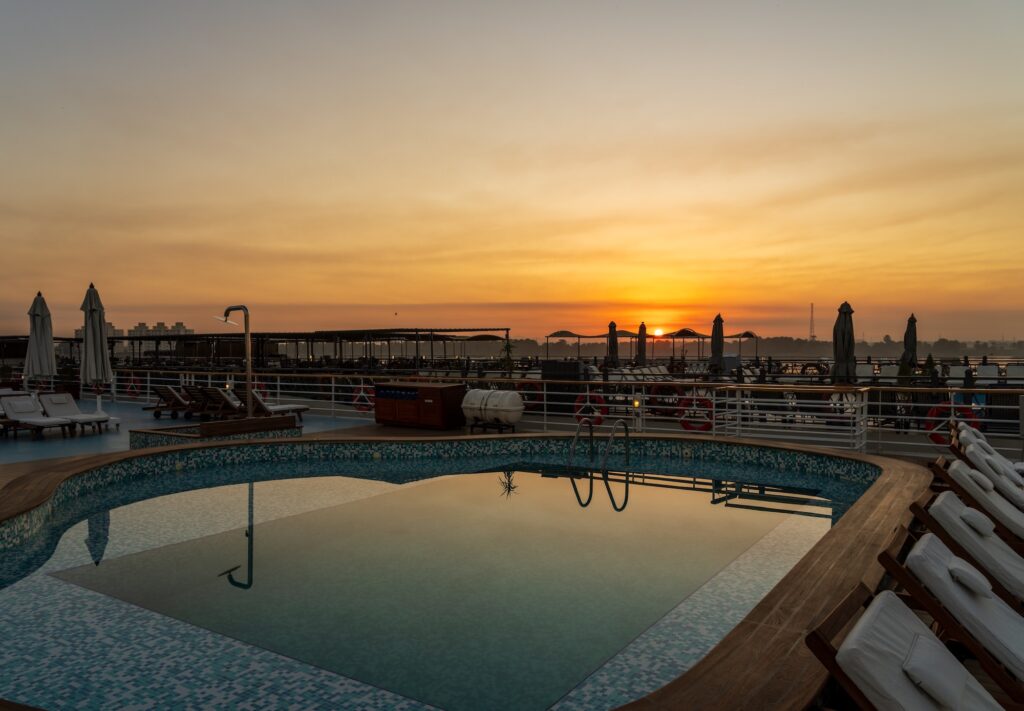 Sunrise over a swimming pool on the deck of a Nile cruise boat docked beside another ship, Nile cruise boat deck swimming pool, Edfu