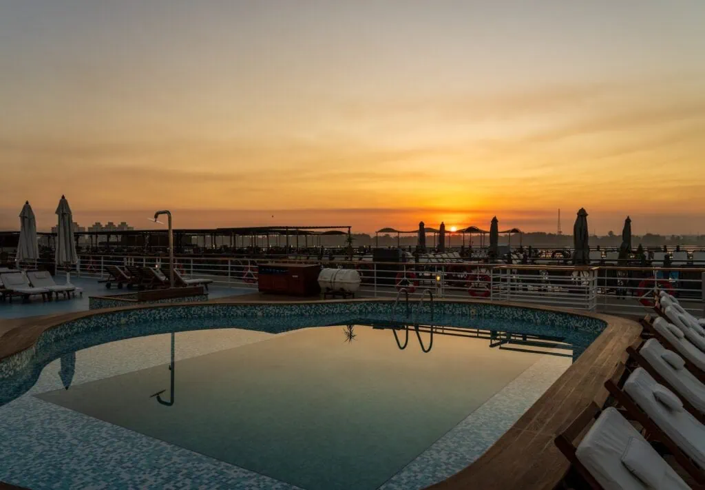 Sunrise over a swimming pool on the deck of a Nile cruise boat docked beside another ship, Nile cruise boat deck swimming pool, Edfu