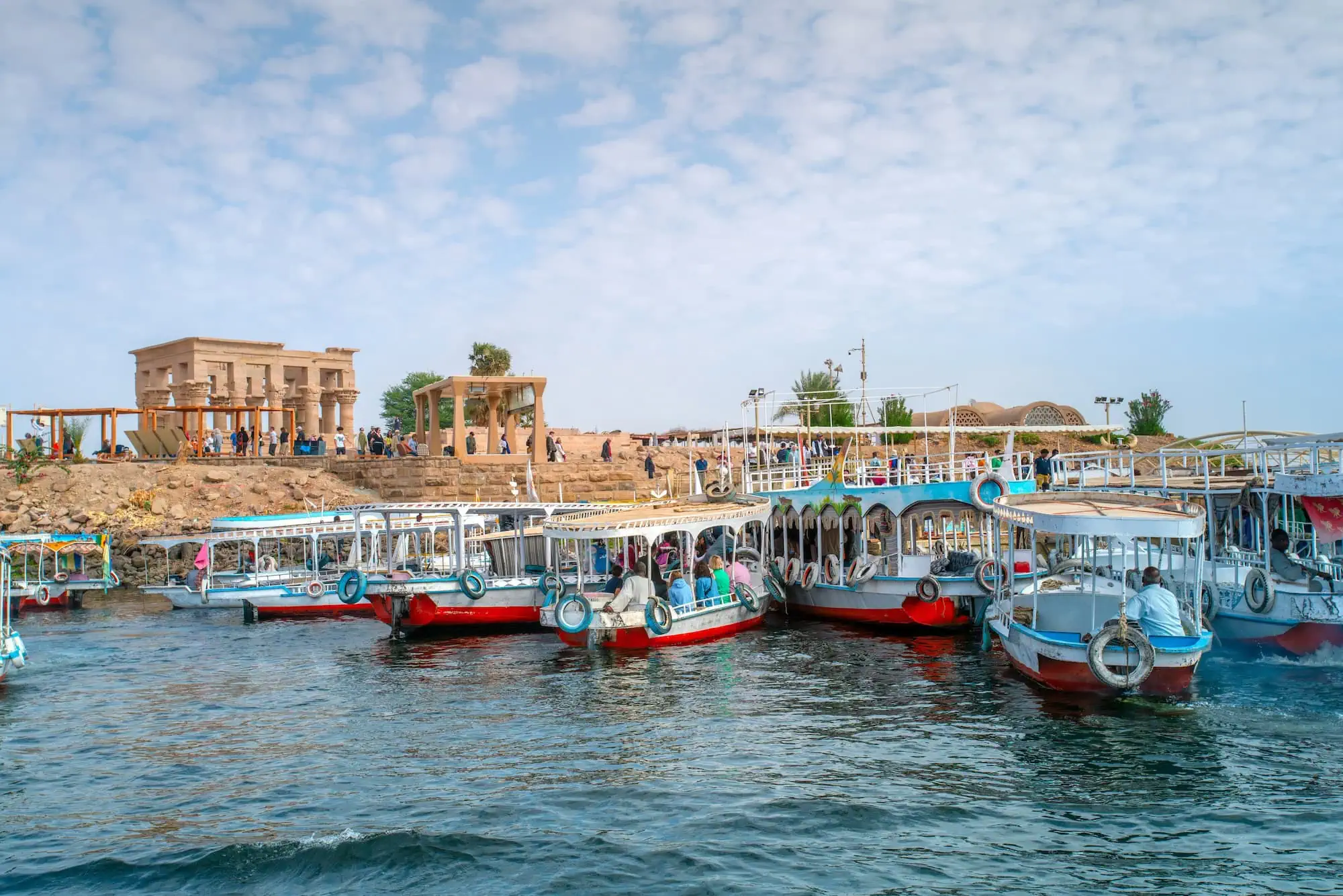 Tourist boats docked at Philae Temple with visitors exploring the ancient ruins