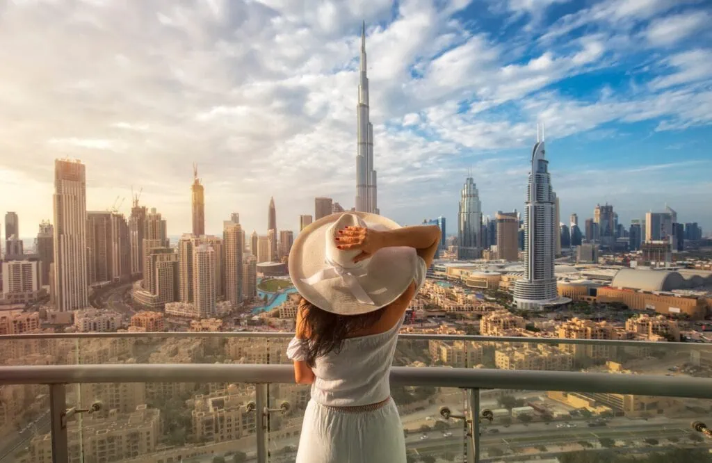 A woman in a white hat on a balcony overlooking the Dubai skyline and its high-rise towers, in the United Arab Emirates, a popular add-on on multi-country Egypt tours.