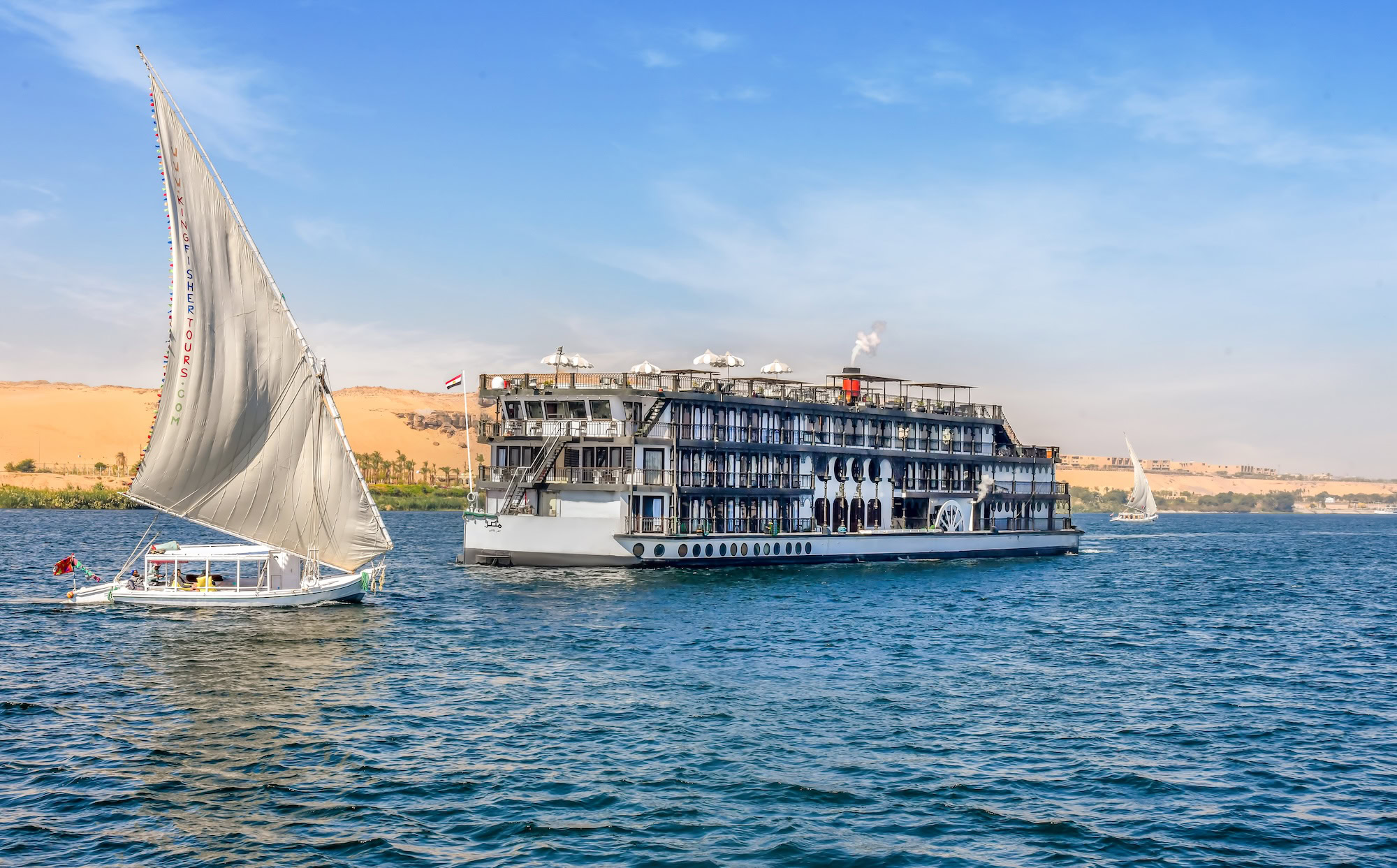 Nile River with cruise ships and traditional sailboat in Egyptian landscape