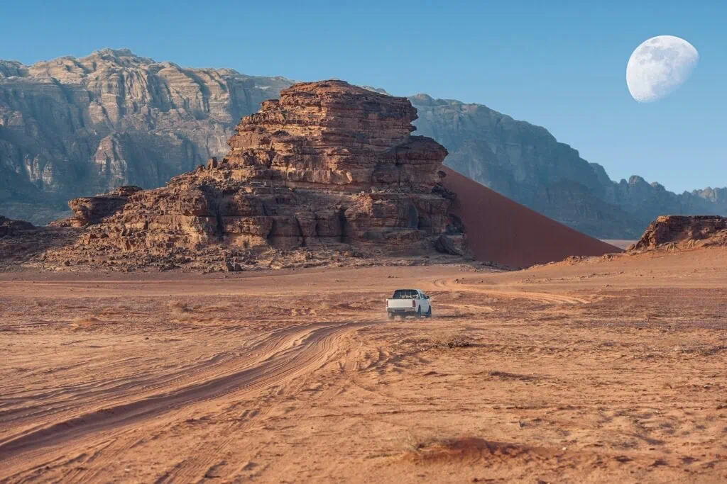 Off-road jeep driving across red sand and rock formations in Wadi Rum, Wadi Rum