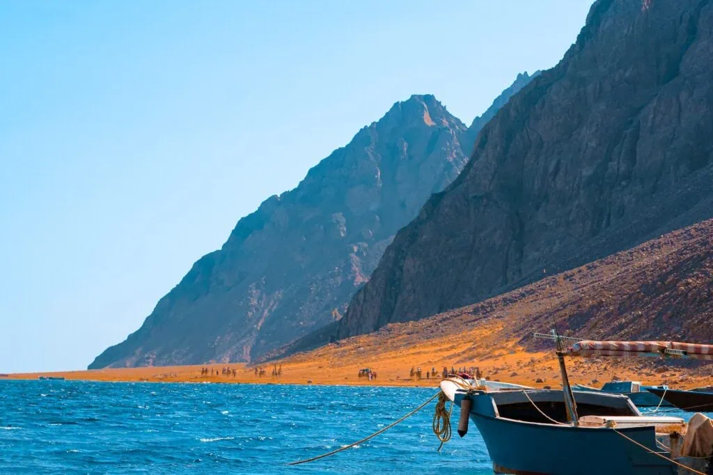 Red Sea Mountains with a small boat on calm blue waters under clear sky, Dahab