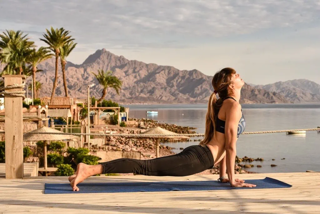 Woman practicing yoga with the Red Sea and rocky mountains in the background, Dahab