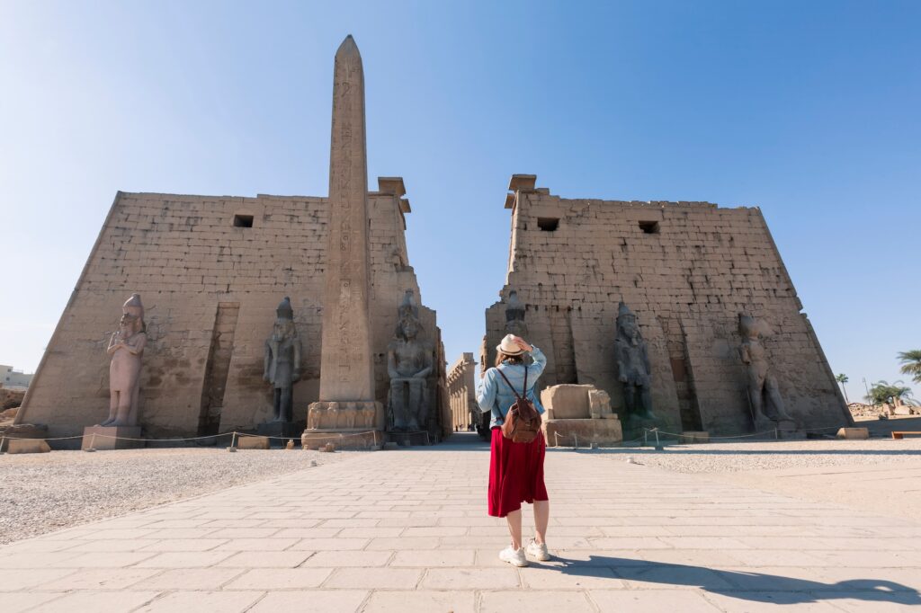 Woman wearing a straw hat facing the entrance pylons and statues of Luxor Temple, Luxor